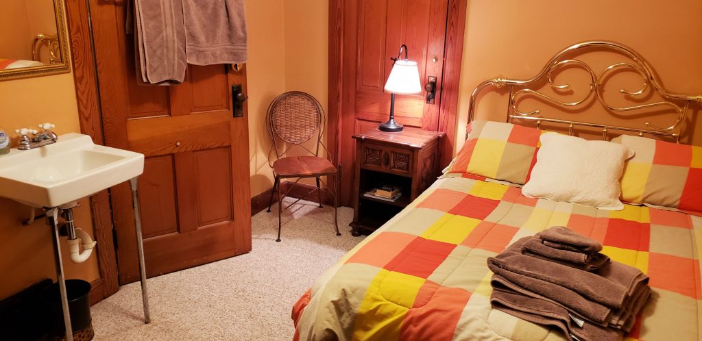 bed with comforter of orange, cantaloupe and lemon colors, in-room sink and wood doors