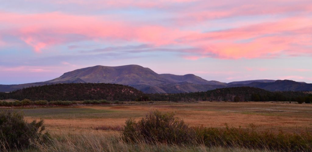cotton candy pink sky over a hump of mountain and grassy prairie in foreground at the Arizona wildlife viewing area