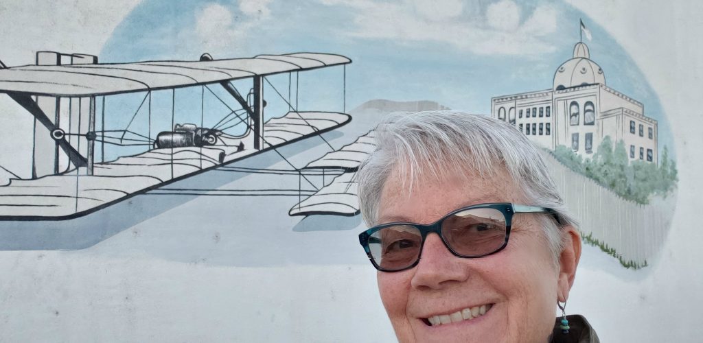 Travel writer Unstoppable Stacey stands in front of wall mural of biplane during Yuma Bird Nature and History Festival