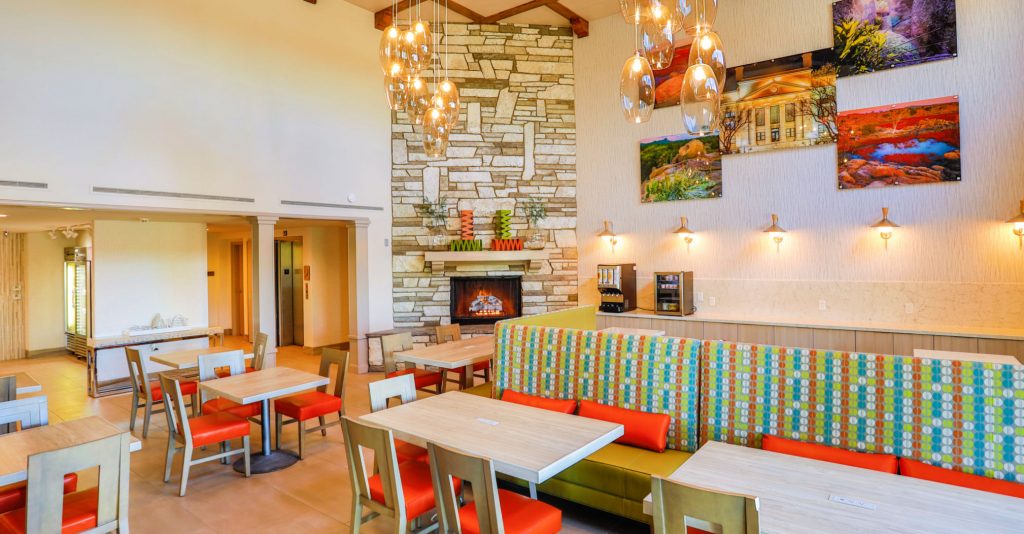 Two-story open room with fireplace, modern lighting fixtures and bright orange chairs at tables