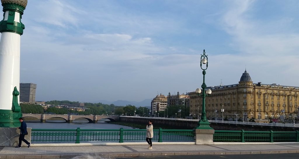 Pedestrians walk across San Sebastian bridge that connects the two parts of town. Wide blue river and arched bridge in background