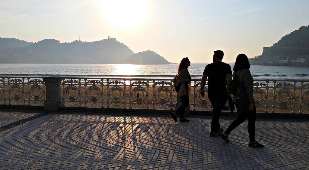 Three people walk siloutted against the sun setting over San Sebastian beach