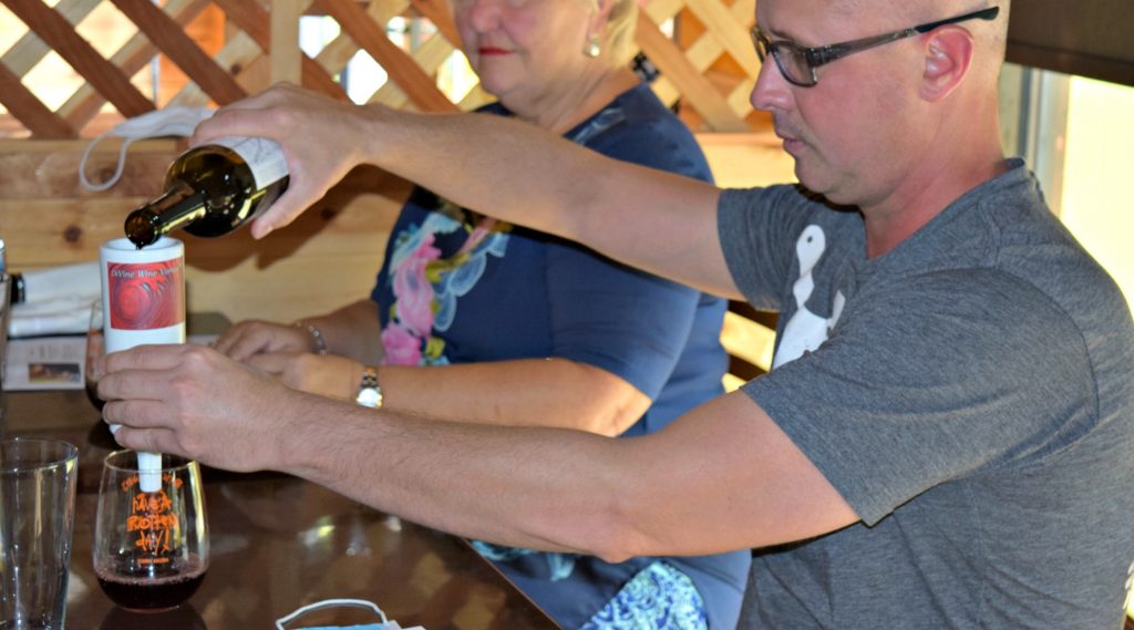 man holds small wine diffuser over glass and pours wine from a bottle into it