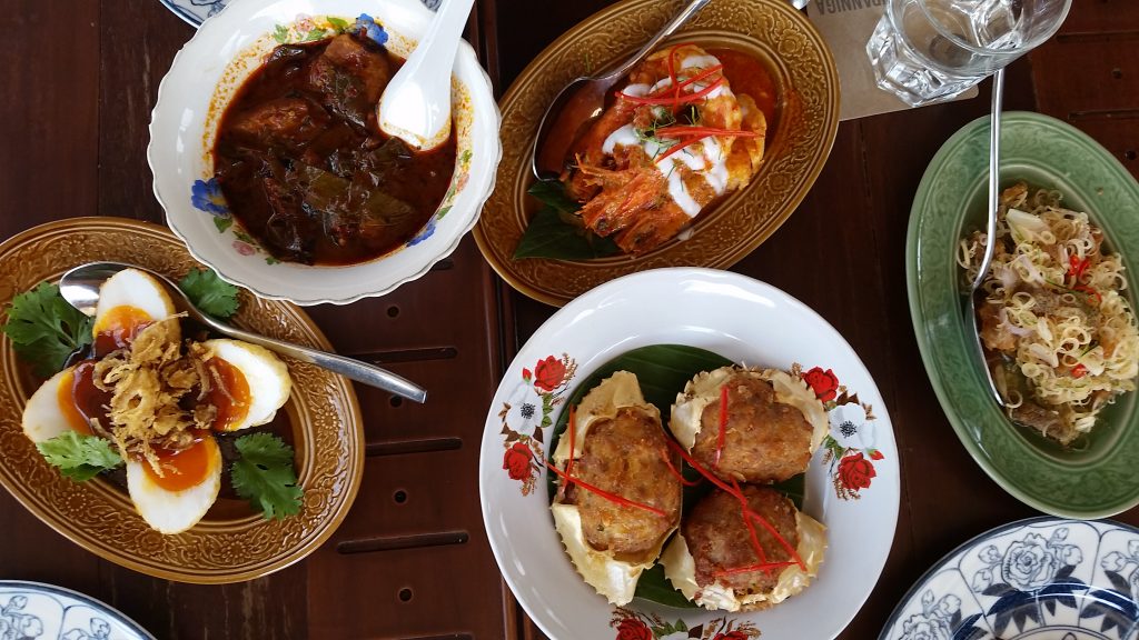 7 Colorful bowls of Thai cuisine are laid out on wooden table.
