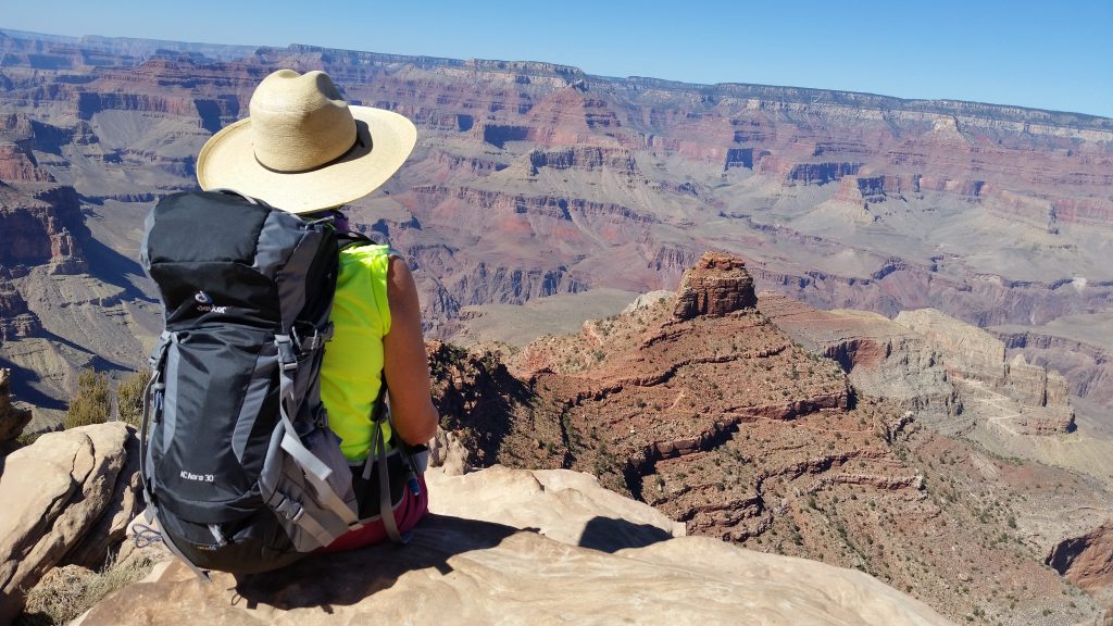 Arizona travel writer Stacey Wittig sits near Kaibab Trail with her back to the camera. She wears backpack and wide-brimmed cowboy hat