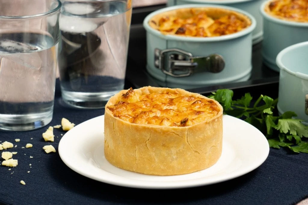 Scottish Macaroni Pie Recipe - Pie on plate with pie tins in background, and glasses of water
