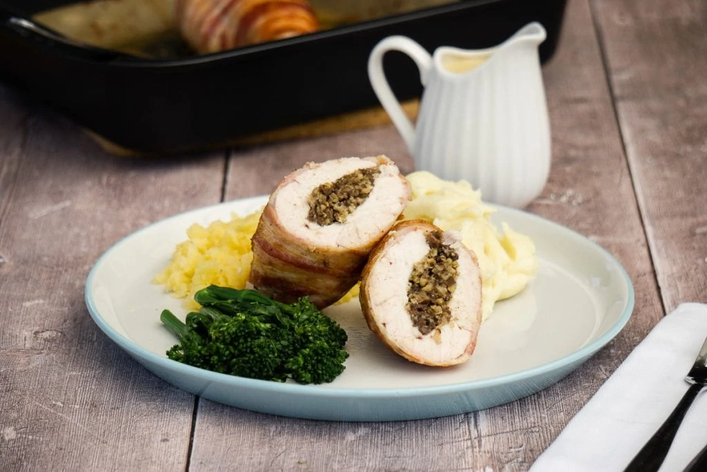 Chicken Balmoral - Chicken stuffed with haggis wrapped in bacon on a plate with vegetables and whisky sauce with oven tray