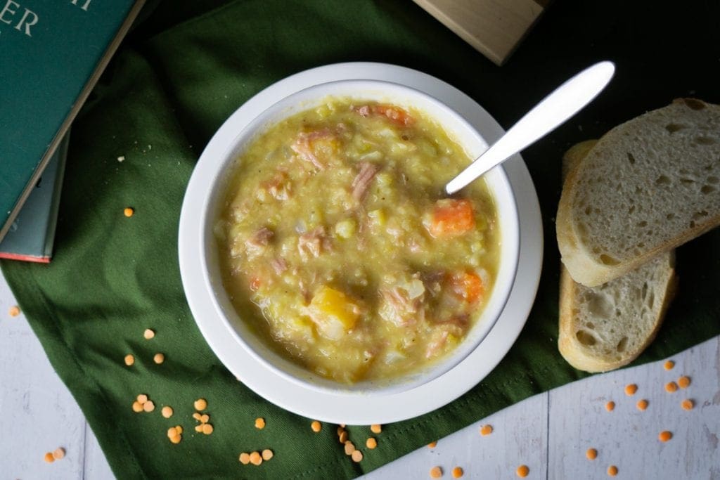 Scottish Lentil and Ham Hock Soup - Lentil and Ham Soup in a bowl with bread and books and lentils scattered about