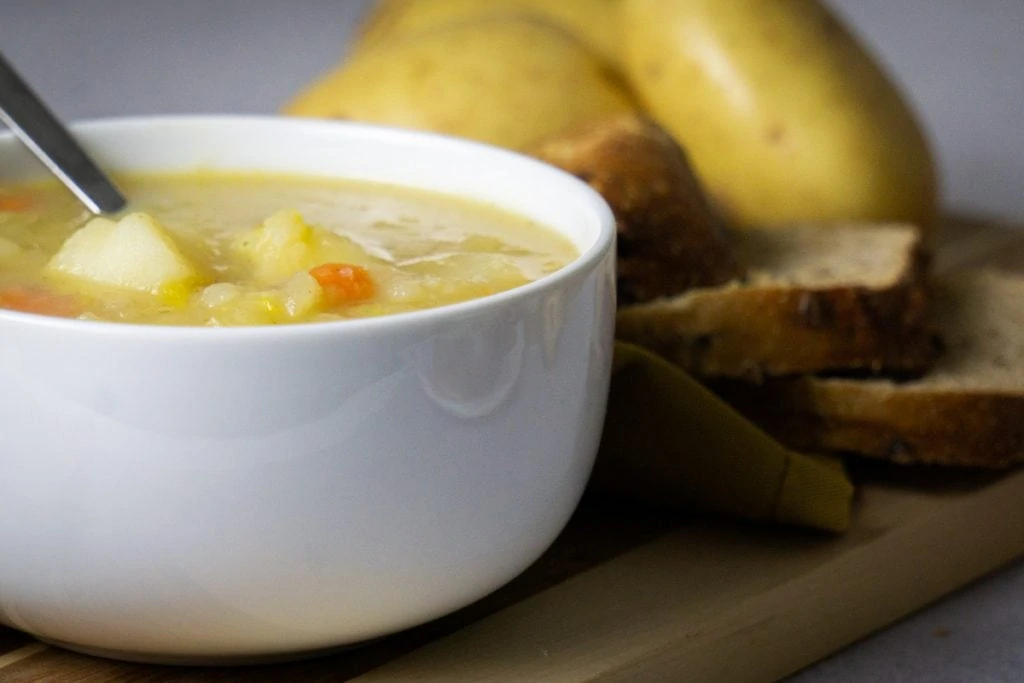 Scottish Potato Soup and Tattie Soup Recipe in a bowl with bread and potatoes beside