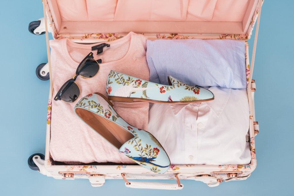Open suitcase with sunglasses, shoes and clothing packed light