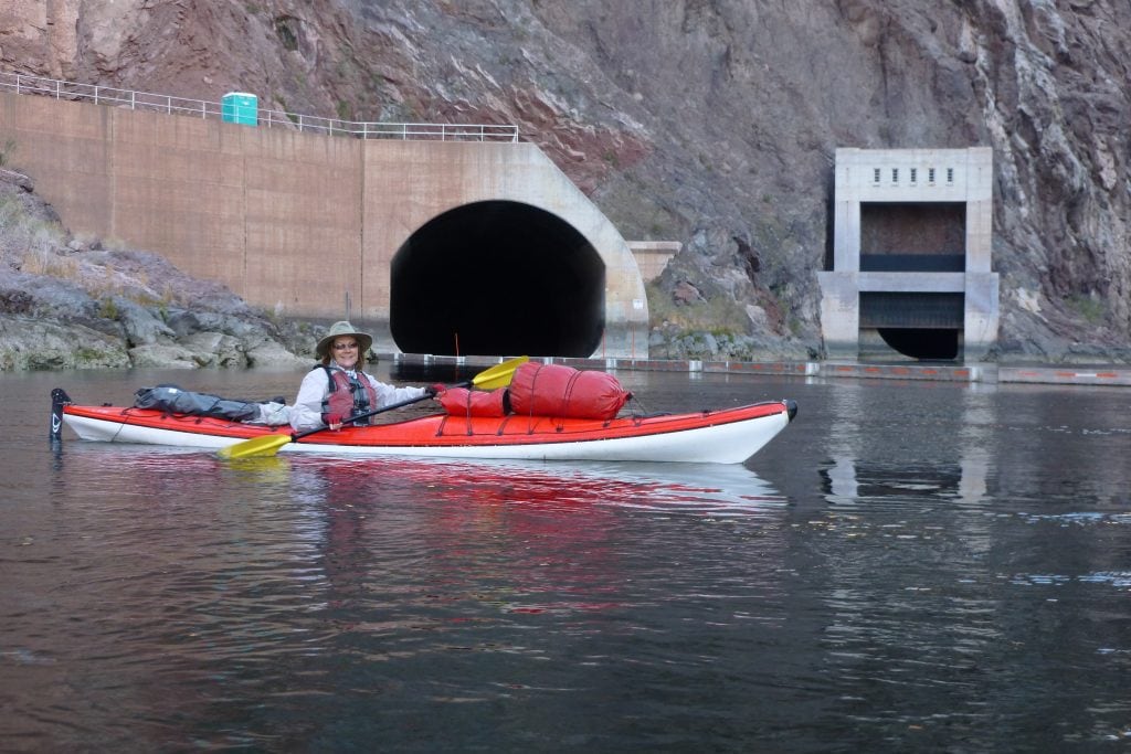 Arizona travel writer Stacey Wittig faces camera while paddling her kayak in front of a huge outlet of a spill tunnel