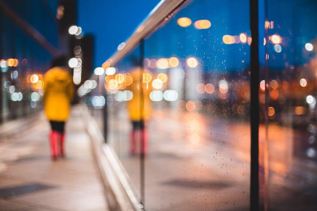 pedestrian wears lightweight rain jacket women's for travel in artisitc streetscape photo with reflections of city lights as night falls during rain