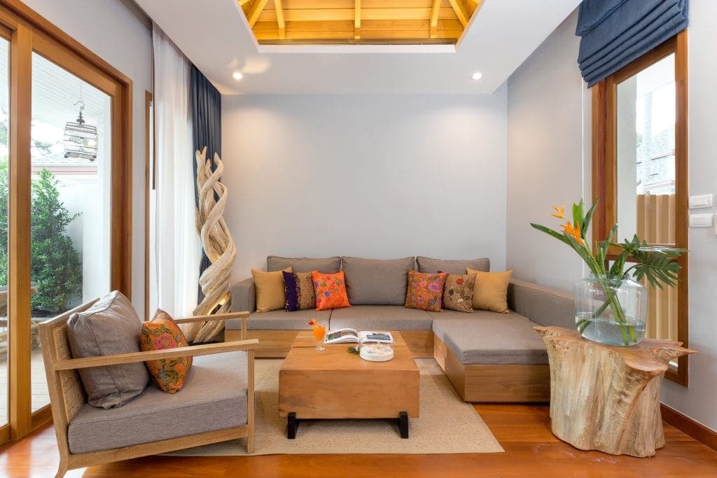 Couch with colorful pillows, upholstered chair with wooden arms, wooden coffee table and area rug in Krabi Resort villa.
