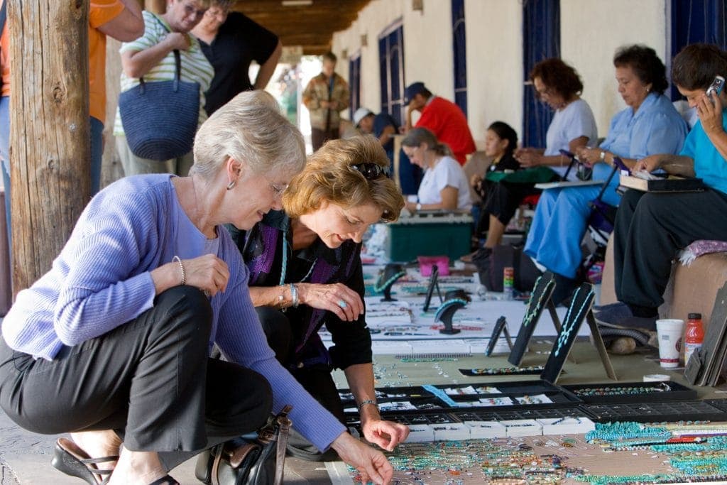 Two middle aged women squat down on Albuquerque sidewalk to view jewelry made by Native artisans