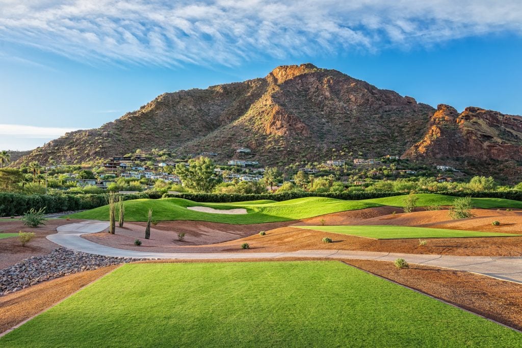 Green golf course in front of red rock mountain with blue skies