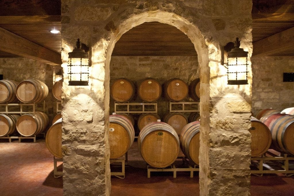 Barrel room of light-colored stone that looks like limestone, romantic lights, barrels of Texas red wine are readt for wine tasting in Texas