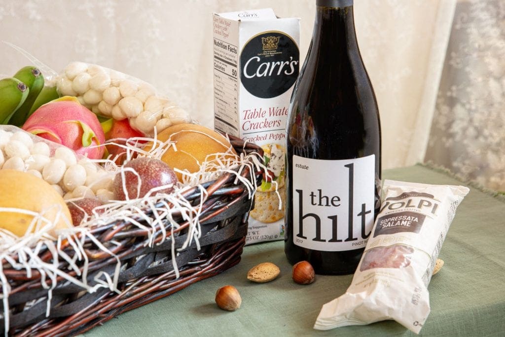 a box of crackers, bottle of Pinot Noir and package of salami sit next to Melissa's Produce gift basket