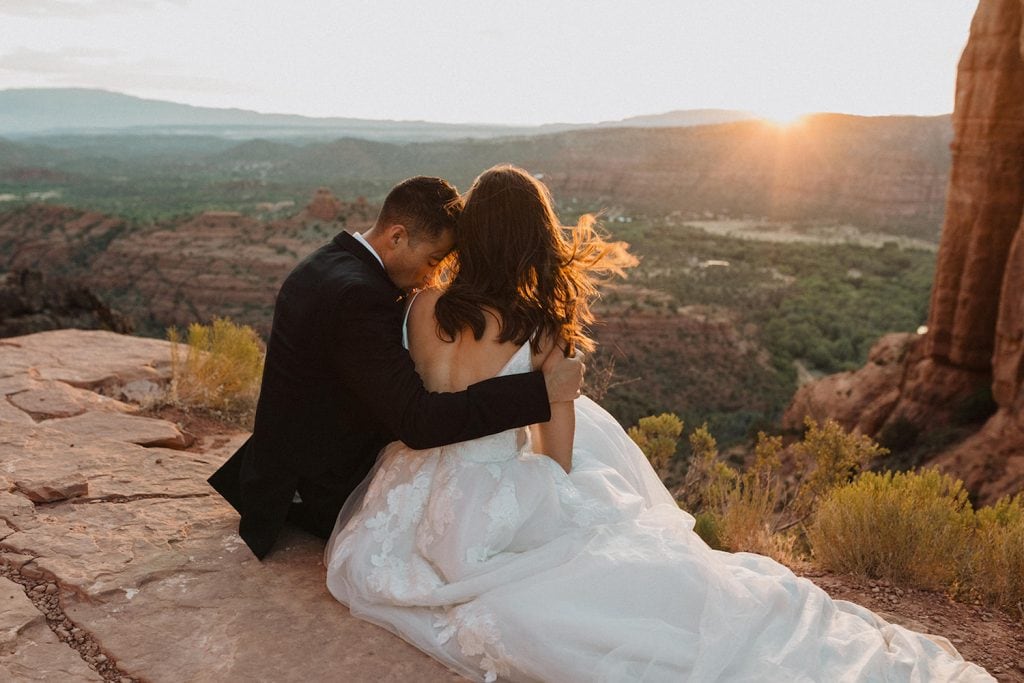 A groom embraces his bride as they sit overlooking the Arizona valley during sunset. Image by Alexa Ann Photography.
