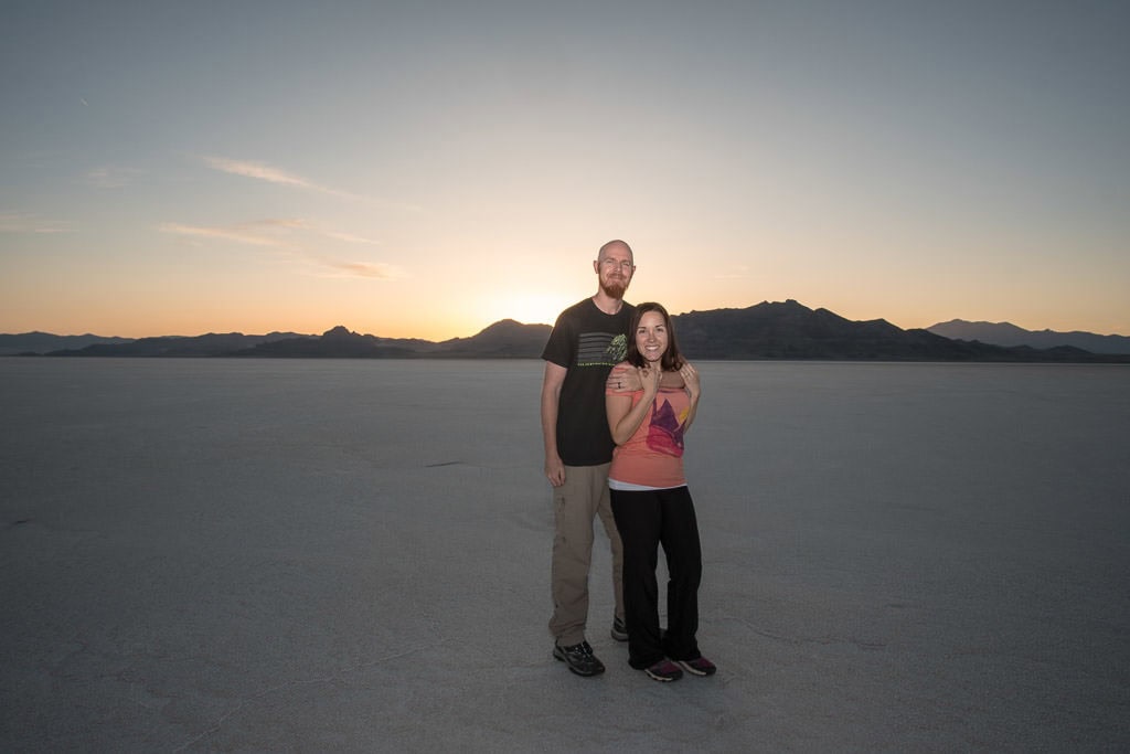 Brooke and Buddy on the bonneville salt flats as the sun sets behind the mountains behind them