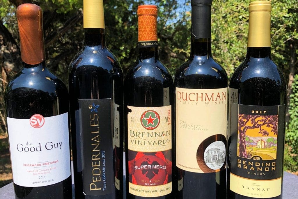 5 bottles of texas red wine sit in front of green trees