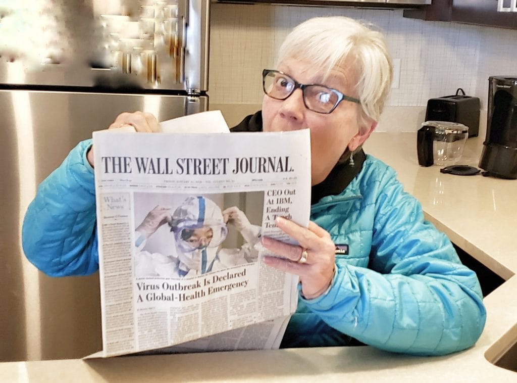 Author looks over edge of Wall Street Journal with large photo of Wuhan Coronavirusworker putting on Hazmat suit