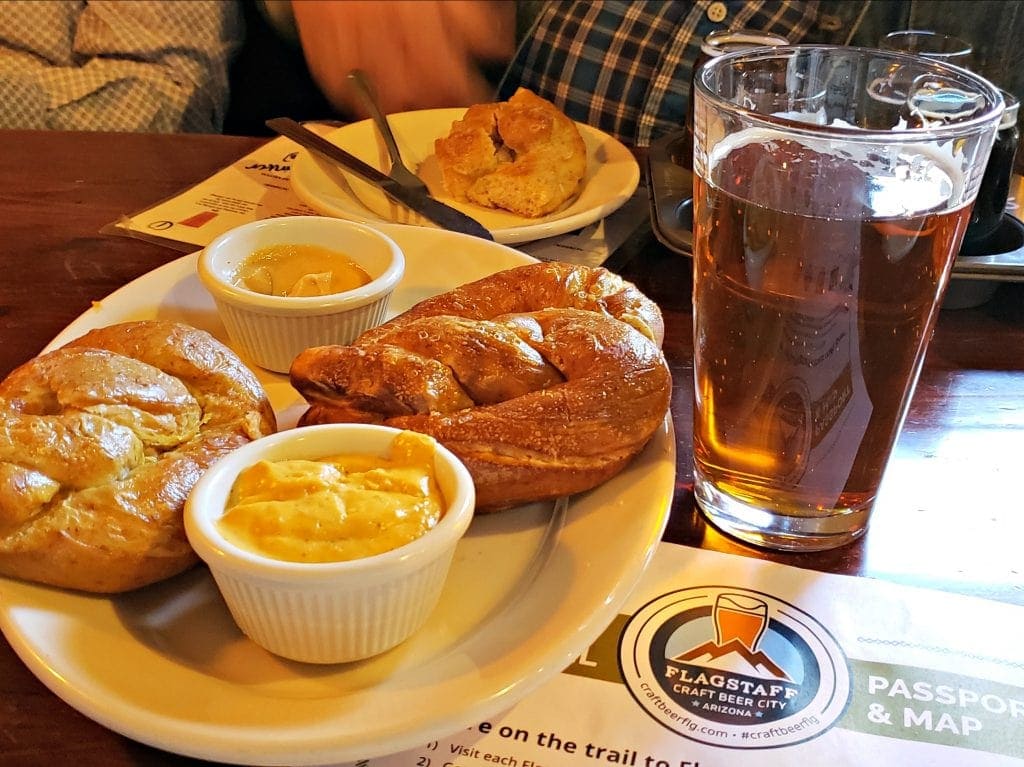 2 pretzels and 2 ramekins of mustard on plate next to red beer at one of the places to eat in Flagstaff
