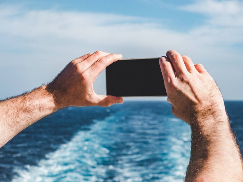 Fashionable man holding a mobile phone on the empty deck of a cruise liner against the backdrop of the sea waves.
