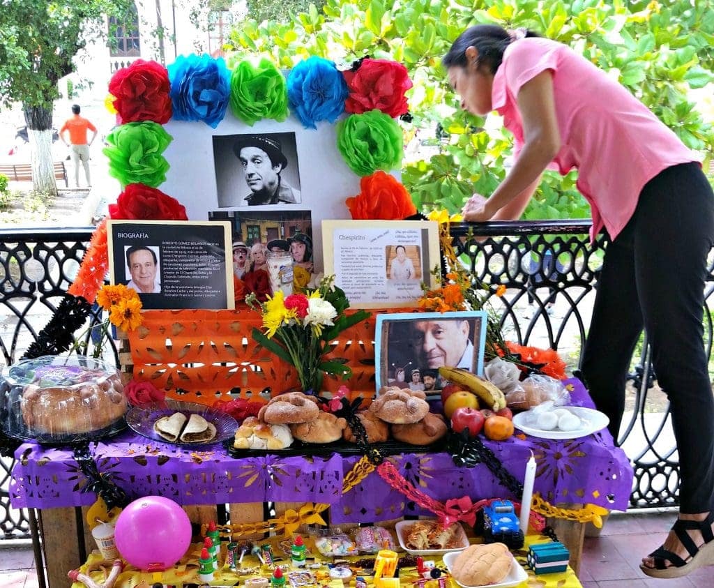Young woman bends over altar with photo of older man framed in crepe paper