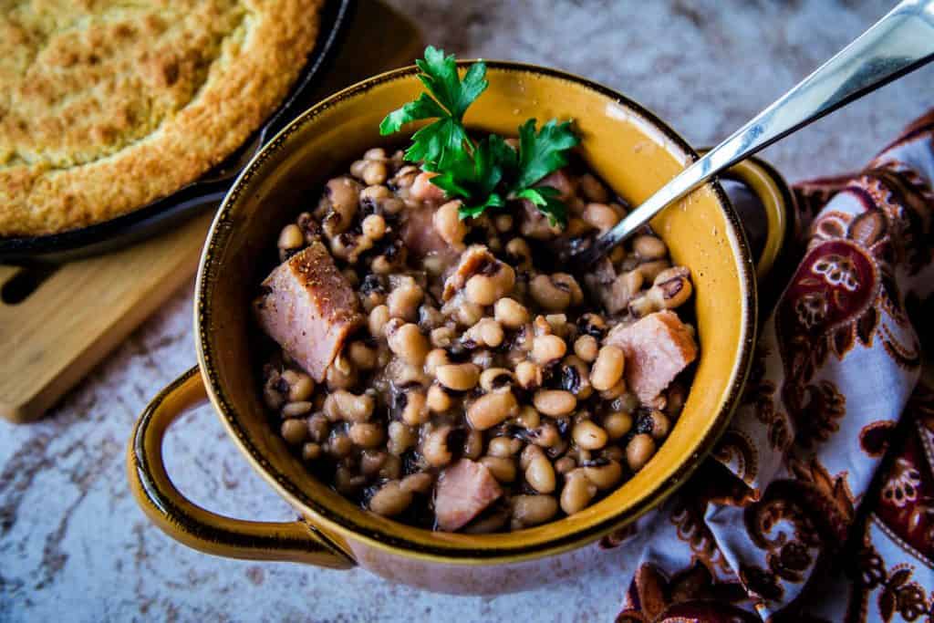 a bowl of black eyed peas with chunks of ham and a skillet of cornbread