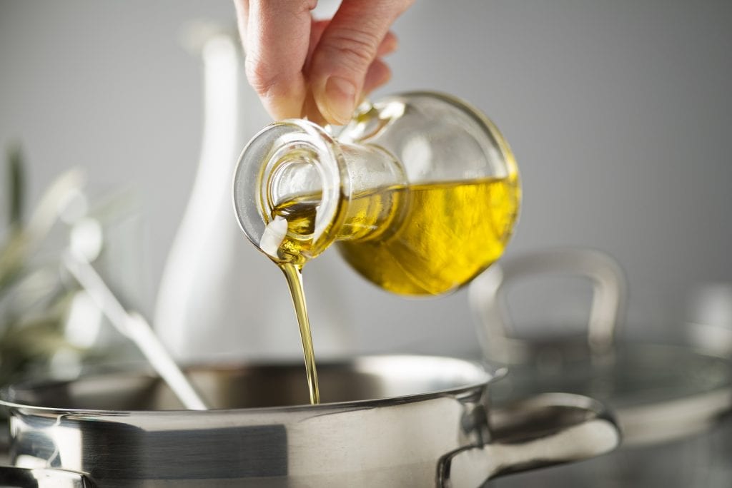 Cooking Meal In A Pot. Bottle Of Extra Virgin Oil Pouring In To
