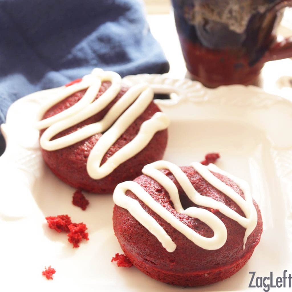 2 red donuts with a white frosting on top on a white plate with a dark blue napkin in the background.