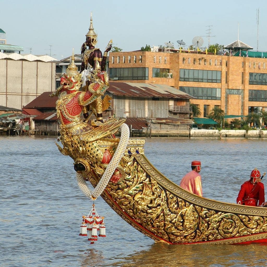 Four armed god - one face dark, the other red faced with gilded wings in the water for the Royal Barge Processional.