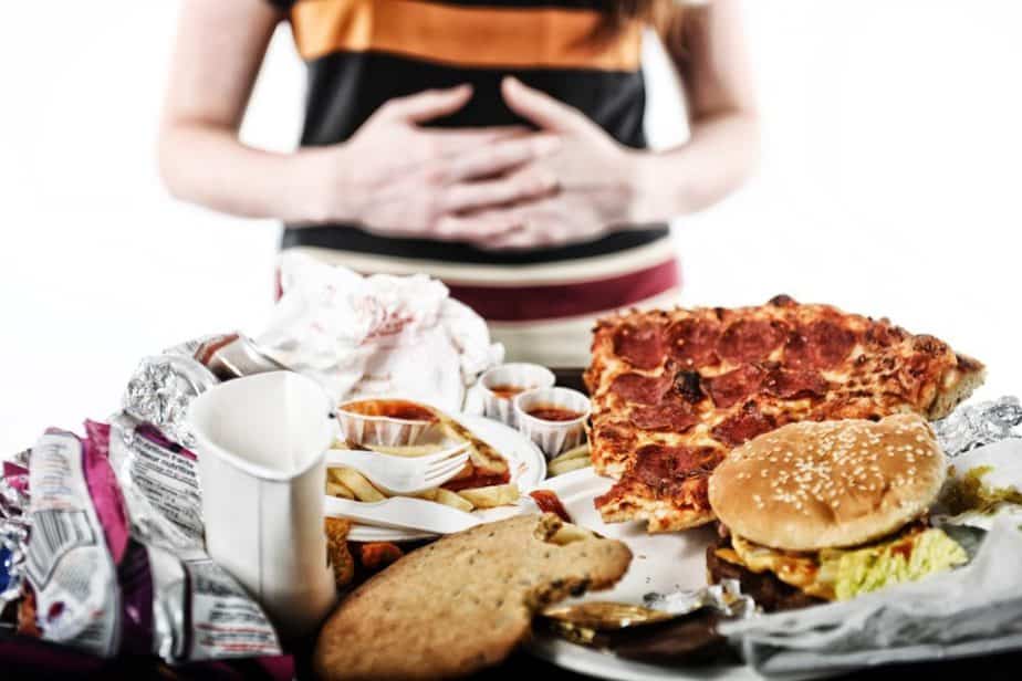 A bloated guy after overeating is having a stomachache, looking at fast food