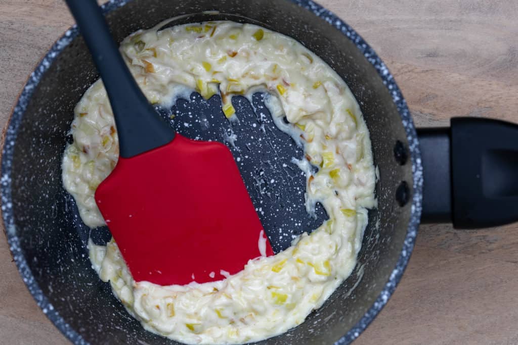 thickened leeks in cream in small saucepan with red spatula