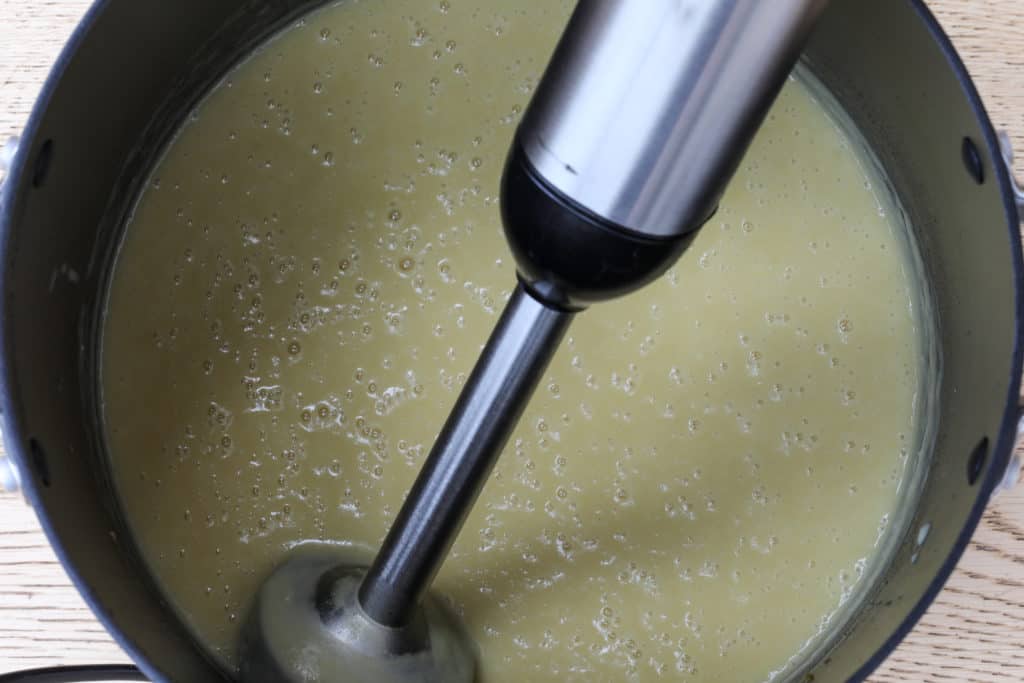 Vegan potato leek soup in pot blended with immersion blender