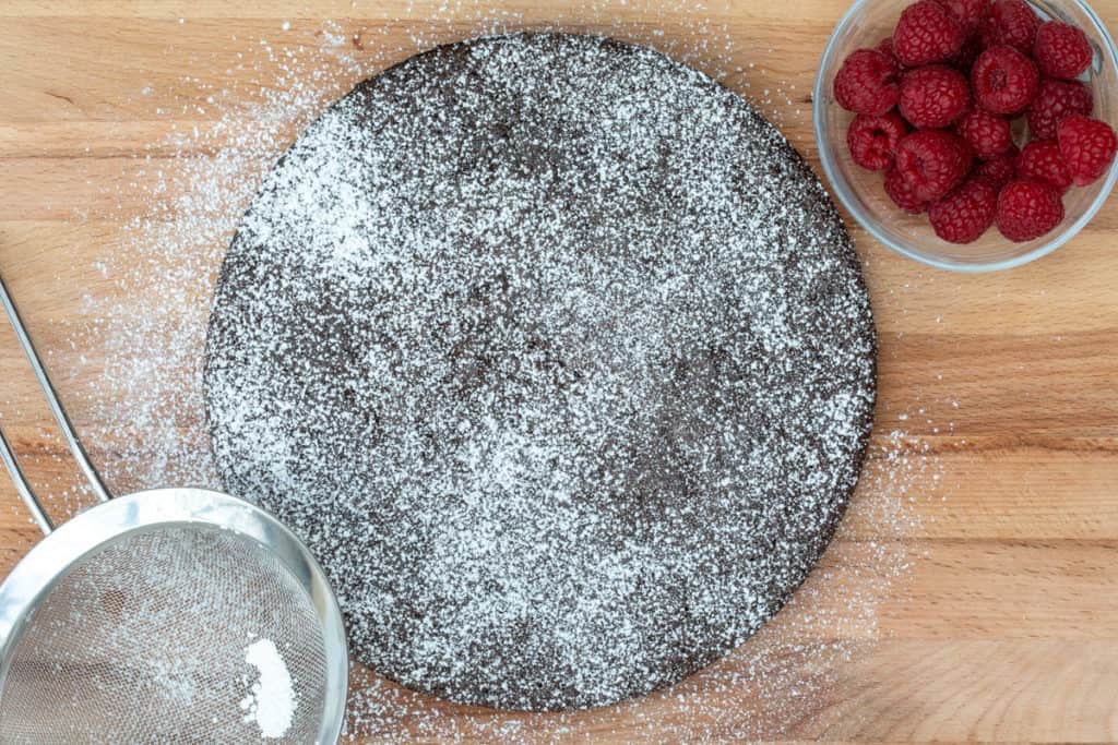 almond flour chocolate cake with bowl of raspberries and powdered sugar