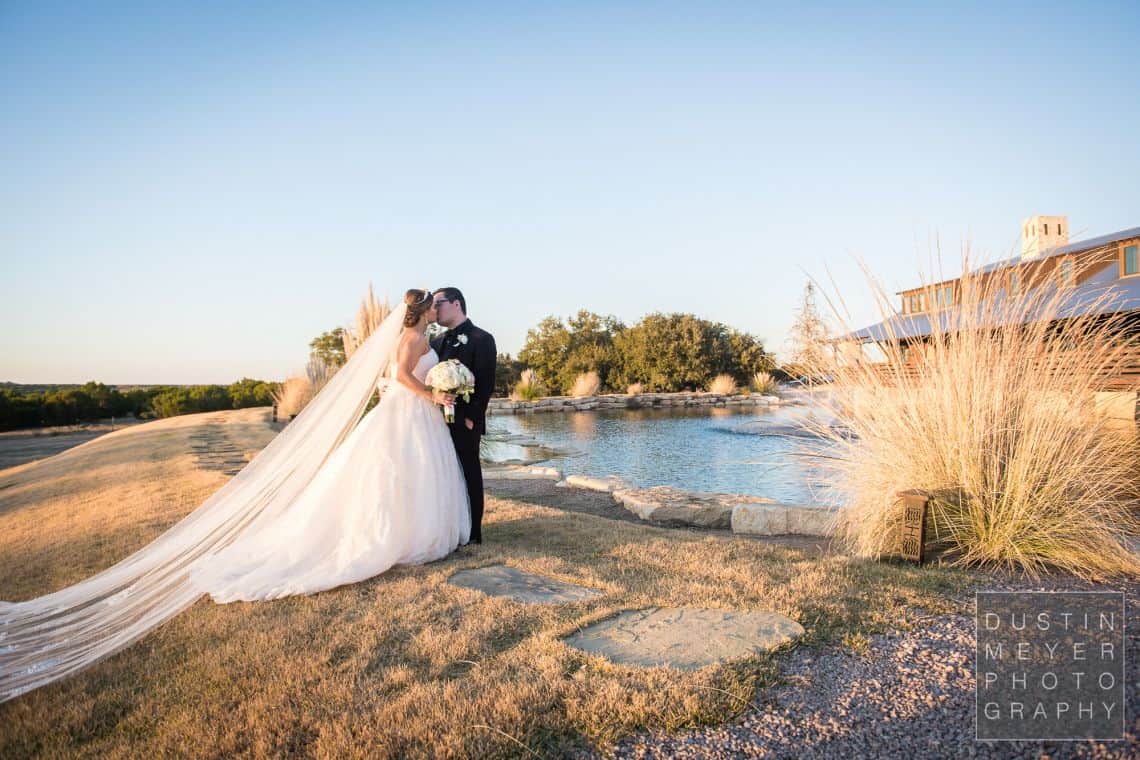 A stunning gorgeous wedding bride and groom next to a lake outdoors in a wedding dress and groom suit