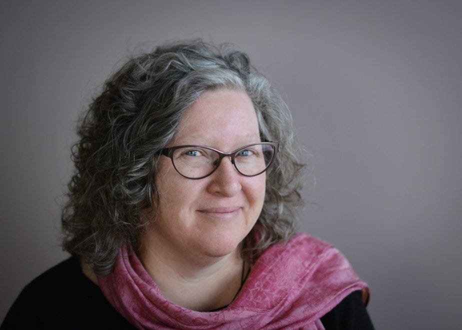 Woman with glasses and pink scarf smiles