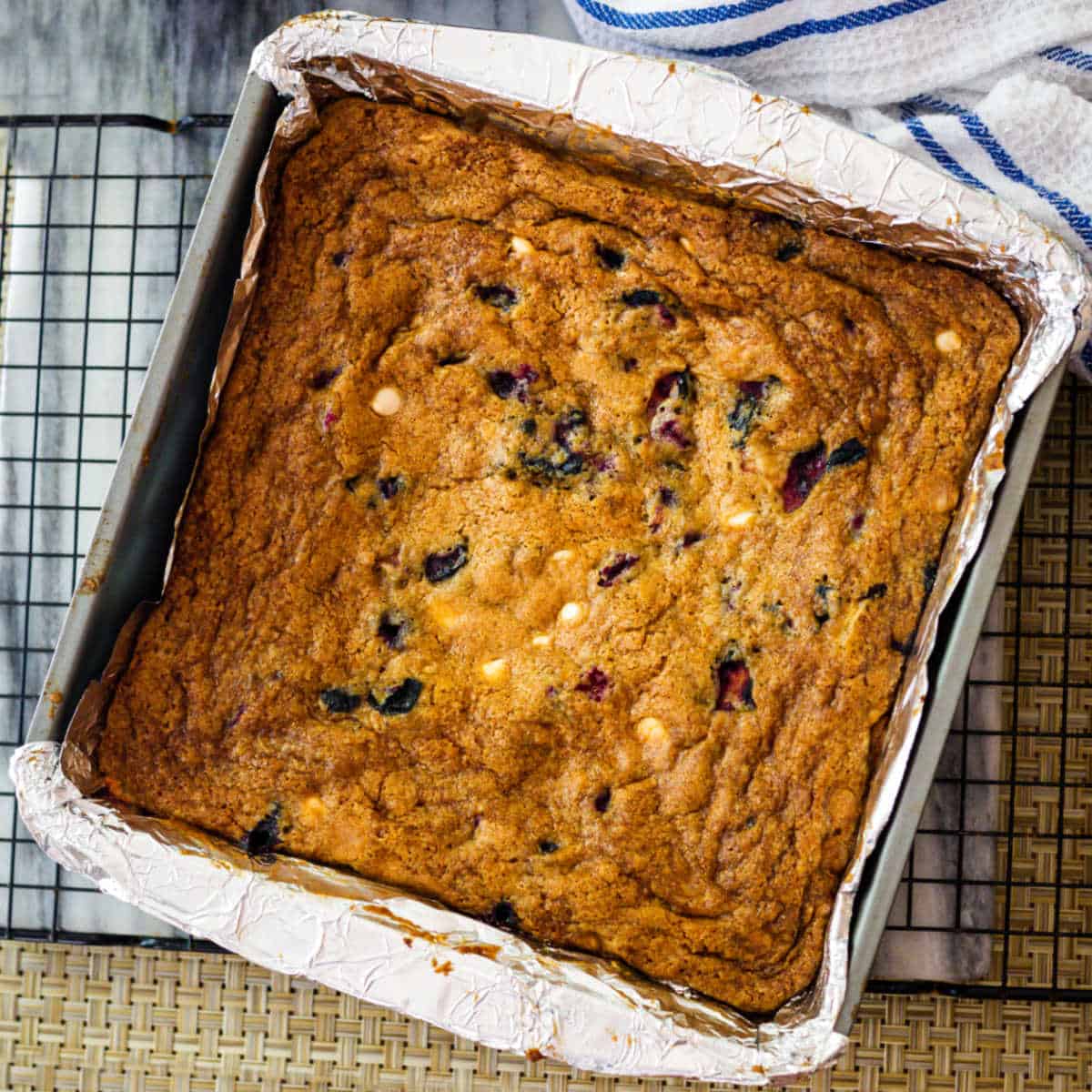 blueberry white chocolate chip cookie bars in an aluminum foil lined pan on a cooking rack