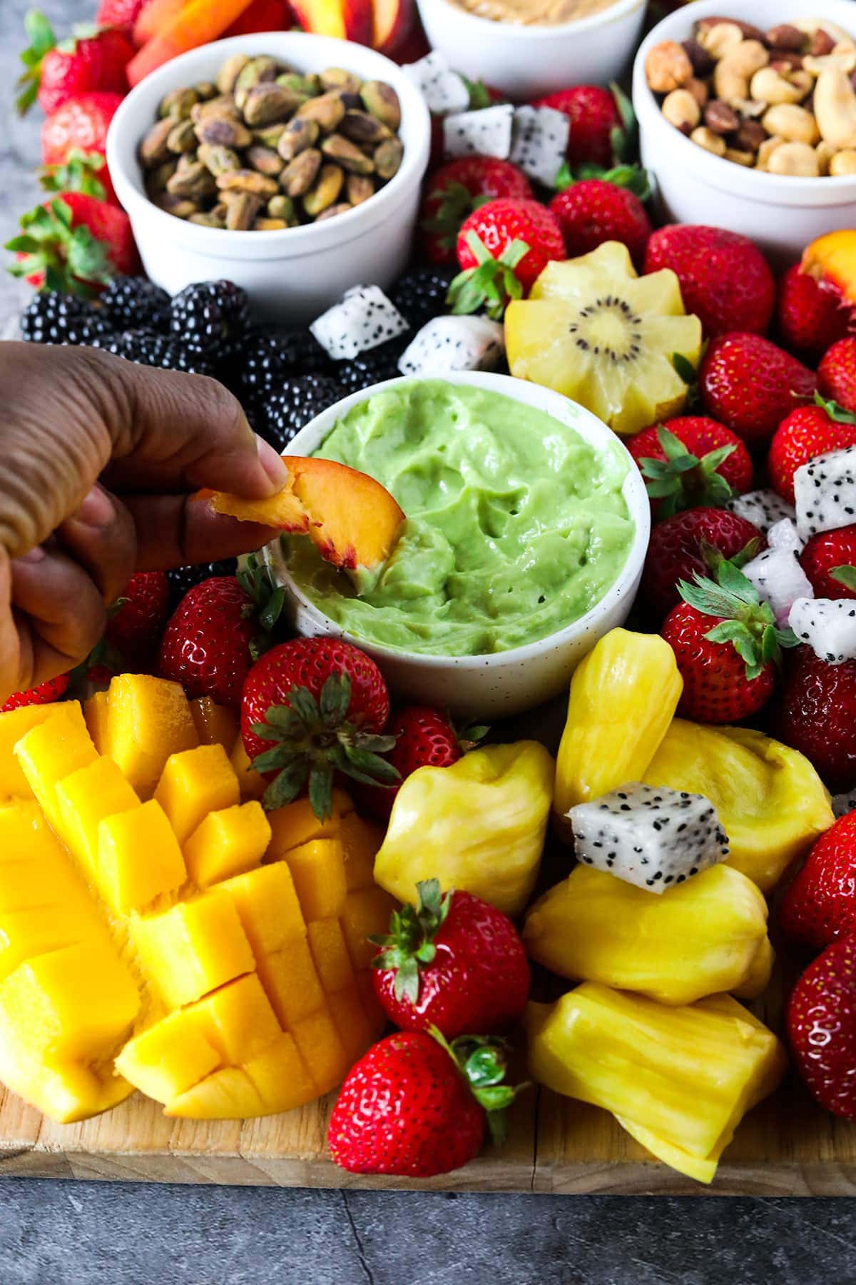 Dipping into vegan key like dip on a cutting board with fruits like mango, peach, strawberries, nuts