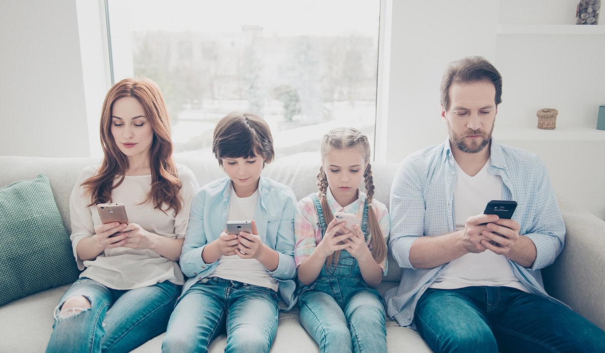 Portrait Of Family With Two Kids Holding Smart Phones Having Electronic Devices In Hands Texting Sms Using Wi Fi 3G Internet Checking Email Searching Contact. Apps Concept
