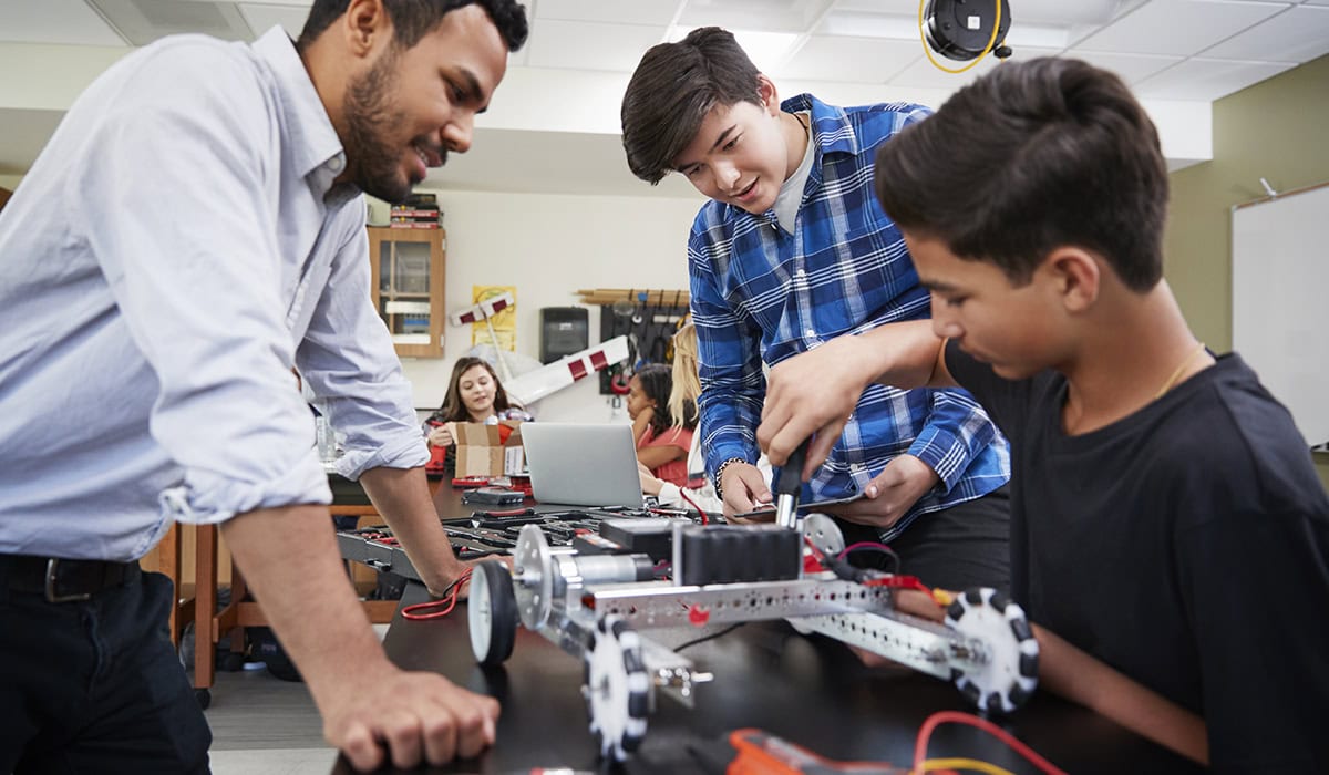 Teacher With Male Pupils Building Robotic Vehicle In Science Lesson