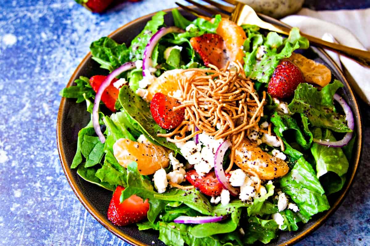 romaine lettuce with red onions, feta cheese, and strawberries in a bowl with a gold fork on a blue background