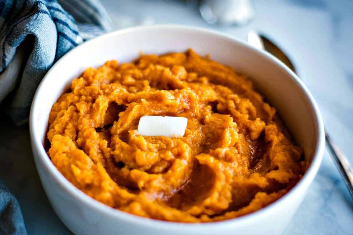Mashed sweet potatoes with a pat of butter in a white bowl