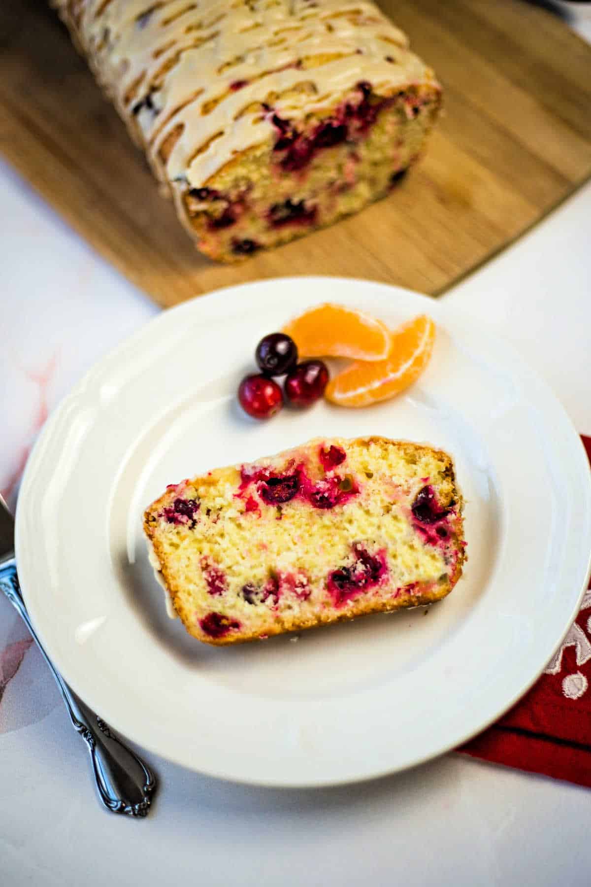a slice of cranberry orange bread on a white plate with orange segments and cranberries