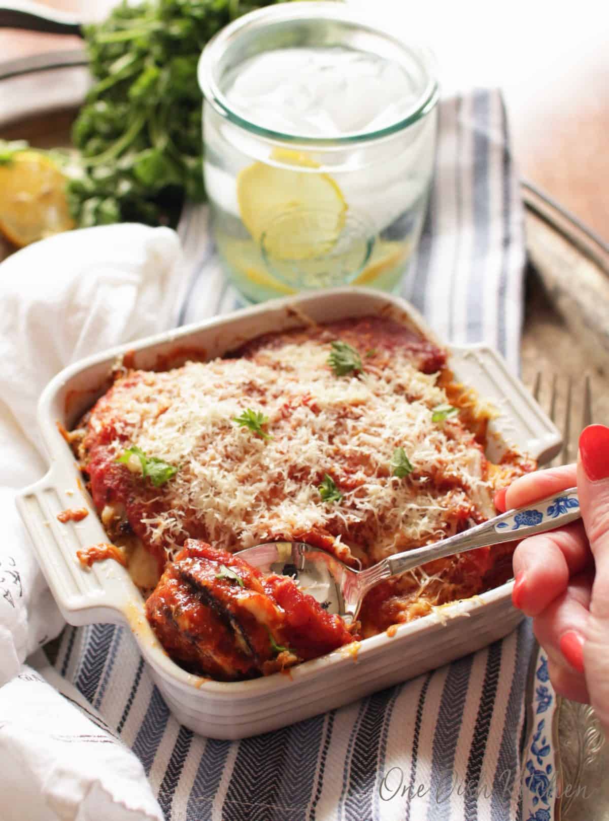 a dish of eggplant parmesan on a blue and white napkin with a fork in the bowl.
