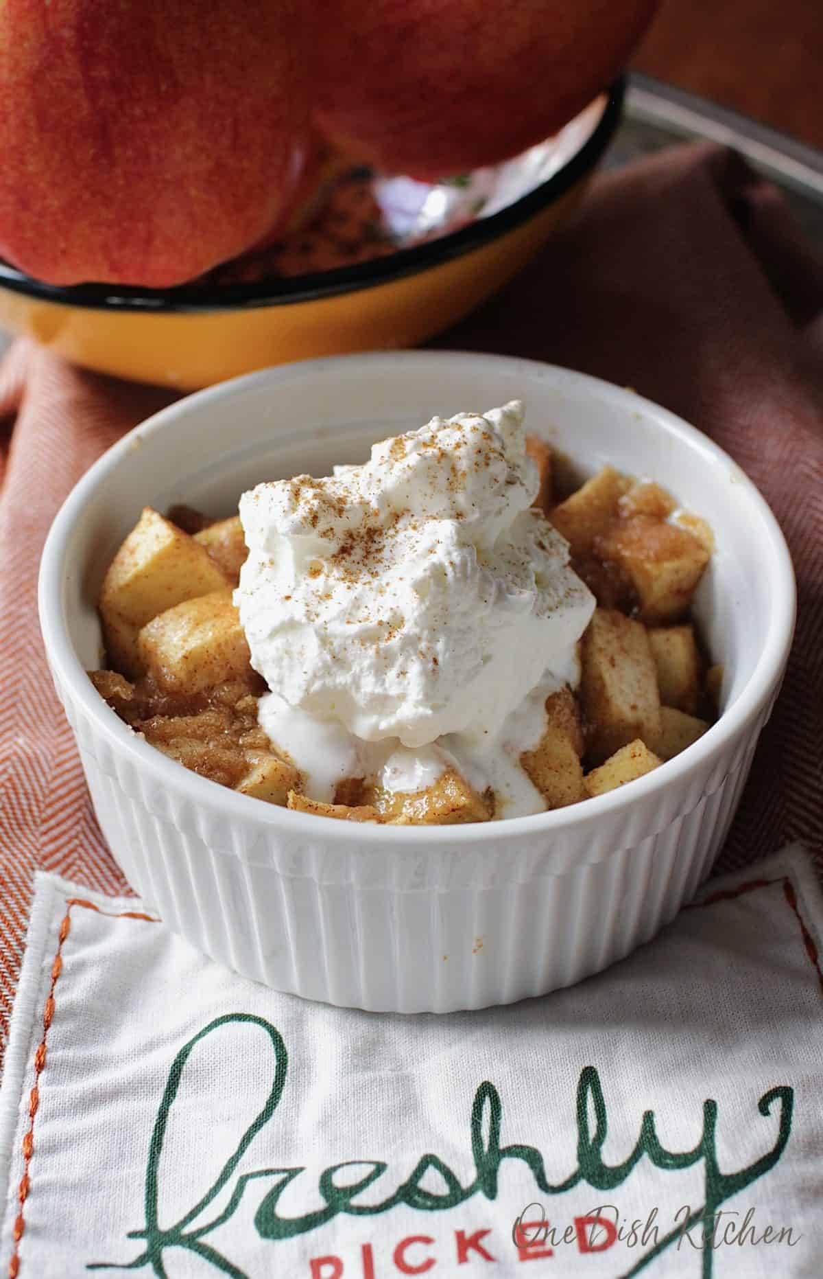 Apple crisp in a ramekin topped with whipped cream and dusted with cinnamon