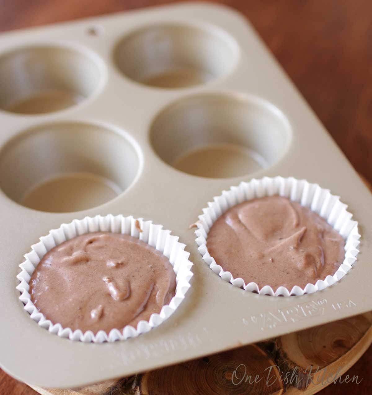 Two cupcake liners filled with cupcake batter in a cupcake pan