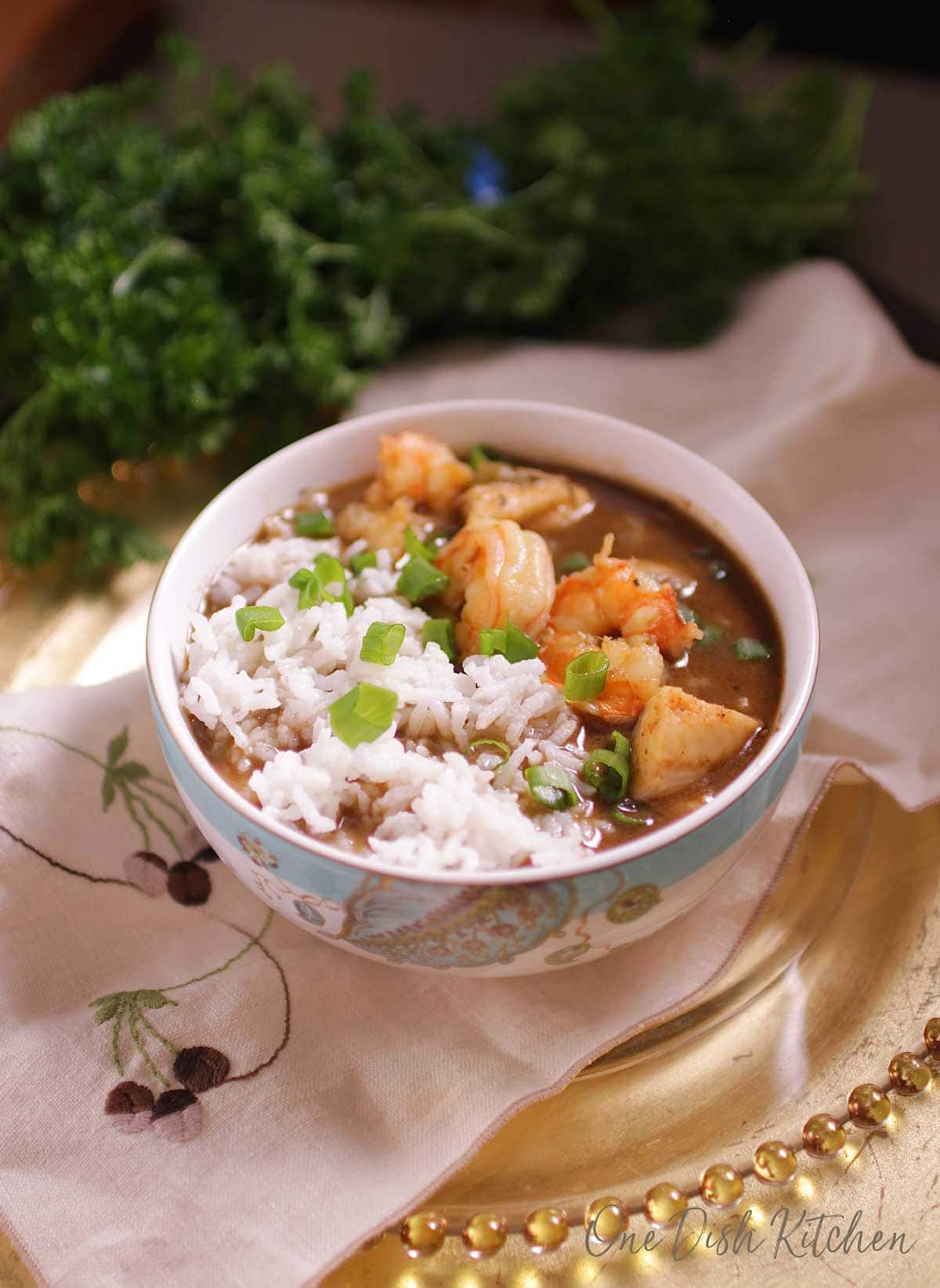 bowl of gumbo with shrimp and white rice on a tray with parsley in the background.