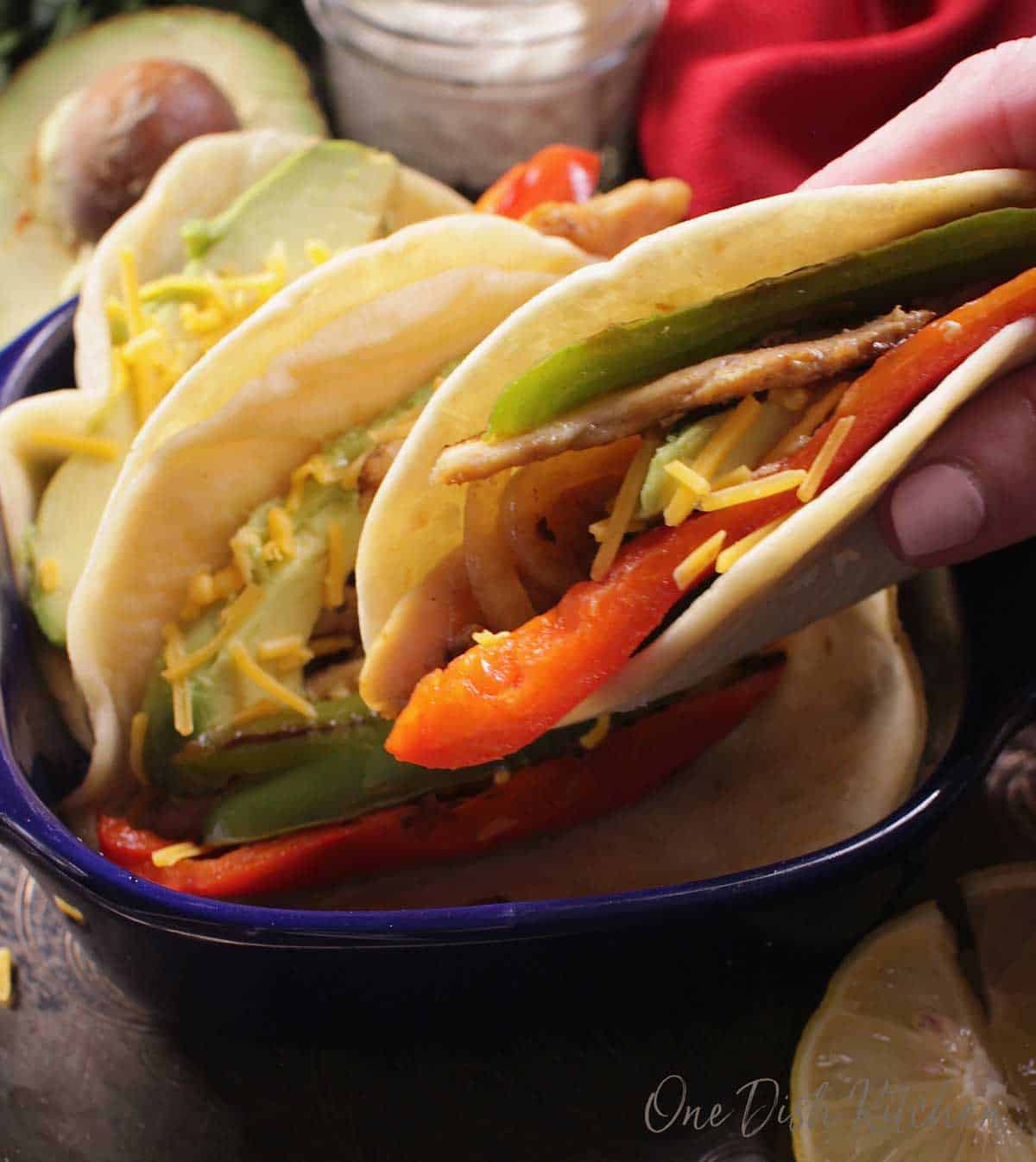 person holding a tortilla filled with cooked chicken, fajita vegetables and shredded cheese.